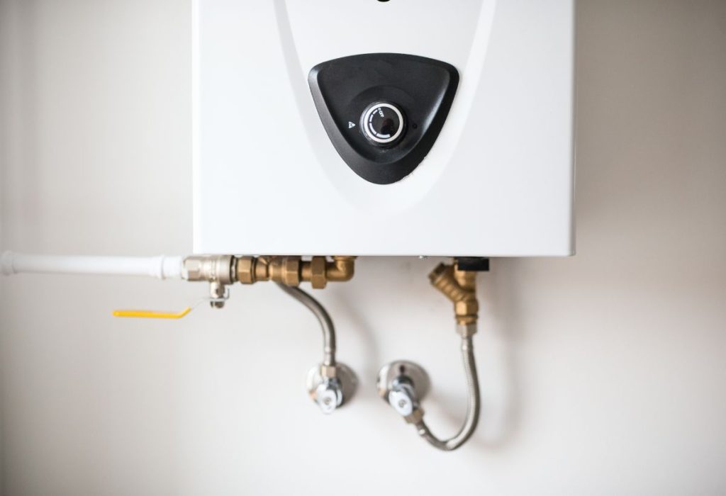 A image displays a modern, wall-mounted tankless water heater, white with a black control panel featuring a central knob