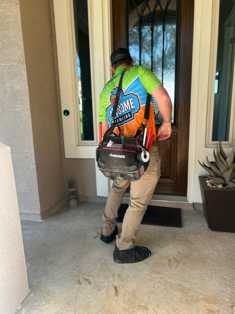 An image of a person, seen from behind, wearing a green, blue and orange t-shirt with text that partially reads "Pawsome Plumbing"