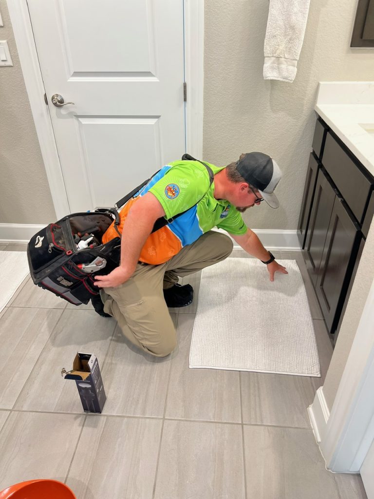 A person inspecting or cleaning something in a bathroom, possibly under the sink or near a vanity
