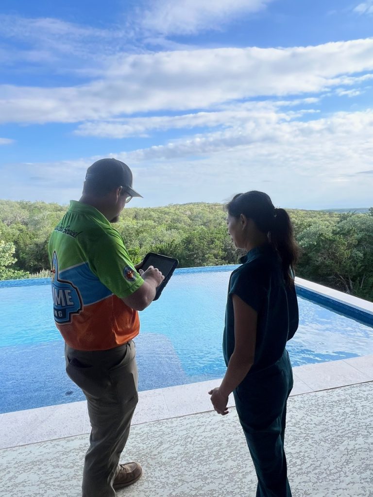 An image of two individuals standing beside a pool, overlooking a vas, green landscape under a partly cloudy sky