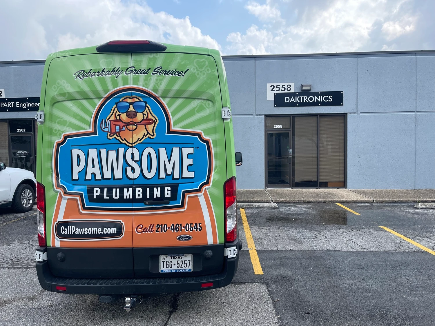 An image of a green and orange plumbing van, prominently featuring the "Pawsome Plumbing" logo with a dog mascot wearing sunglasses and holding a wrench