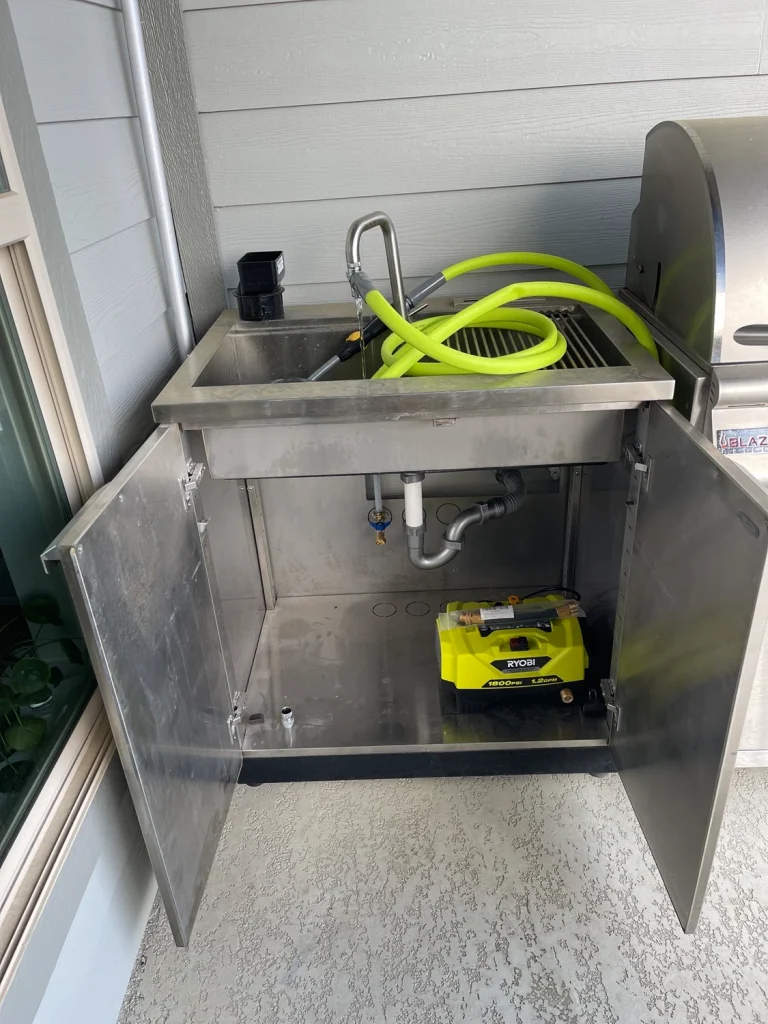 An image displays an stainless steel sink unit with two open cabinet doors revealing a yellow object inside